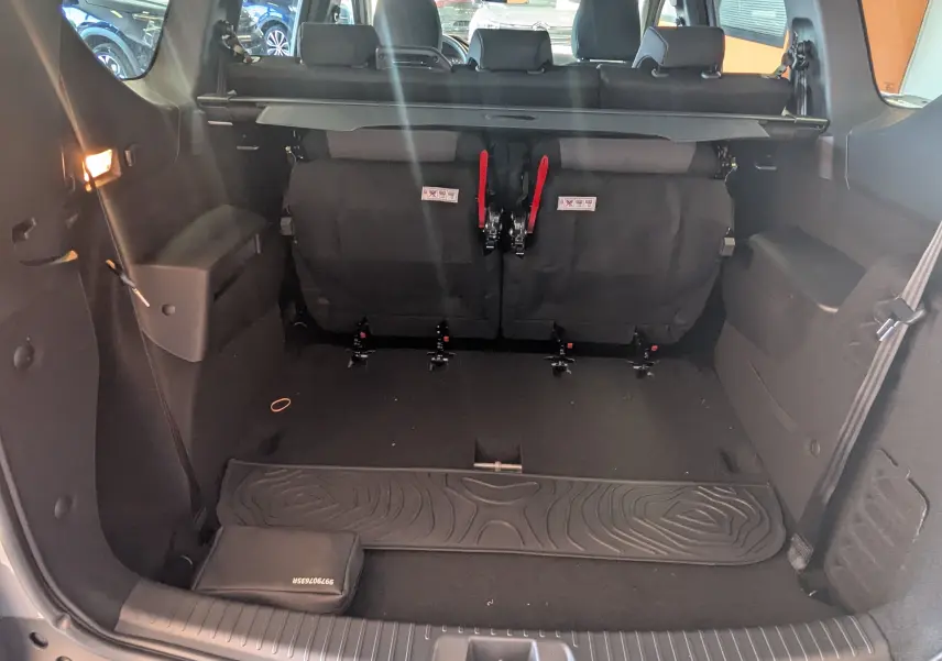 Coffre ouvert du Dacia Jogger gris schiste métal, vue arrière montrant la troisième rangée de sièges rabattue et l'espace de chargement.