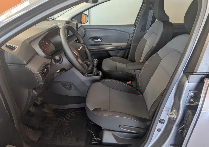 Intérieur avant droit du Dacia Jogger gris schiste, sièges tissu noir avec surpiqûres, volant multifonction et boîte manuelle.