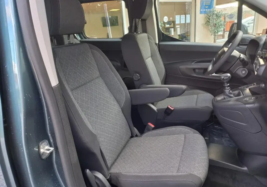 Vue intérieure côté gauche de l’Opel Combo Life Elegance M 2025 bleu, montrant les sièges avant en tissu gris et la boîte manuelle.