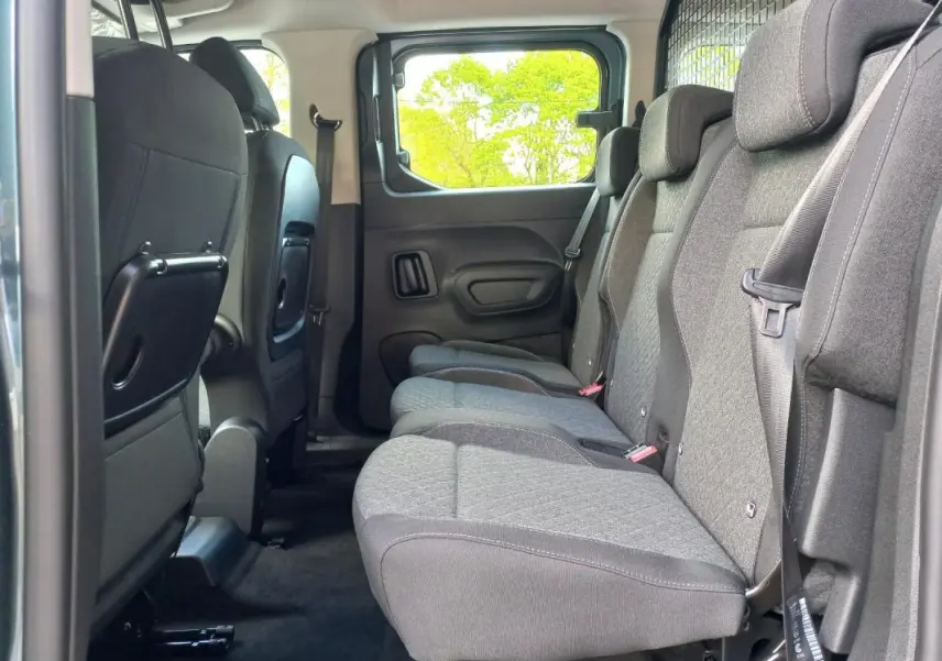 Vue latérale intérieure sur les sièges arrière gris du Opel Combo LIFE Elegance M 2025, avec tablette rabattable au dos des sièges avant.