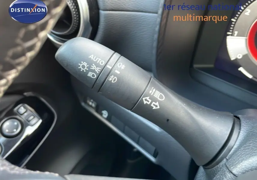 Gros plan sur la commande des feux et clignotants à gauche du volant dans l’habitacle noir du Nissan Juke 2025.