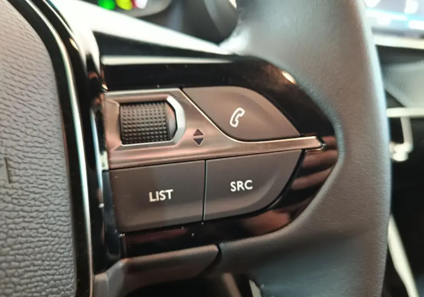 Gros plan sur les commandes multifonctions en cuir du volant côté gauche du Peugeot E-2008 électrique gris clair.