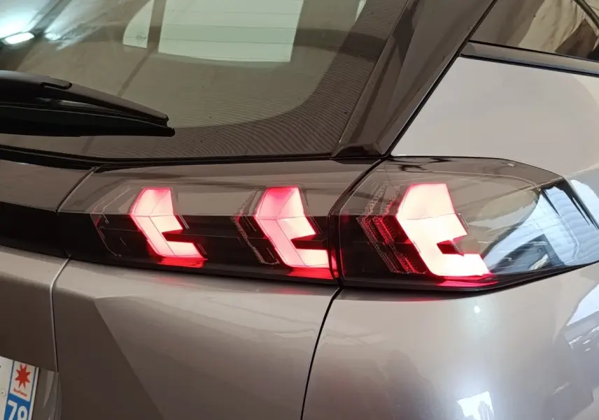 Gros plan sur le feu arrière droit allumé d’un Peugeot E-2008 électrique gris clair 2023.