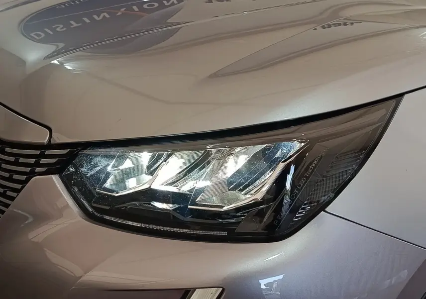 Gros plan sur le phare avant droit du Peugeot E-2008 électrique gris clair, mettant en valeur les détails LED et la calandre.