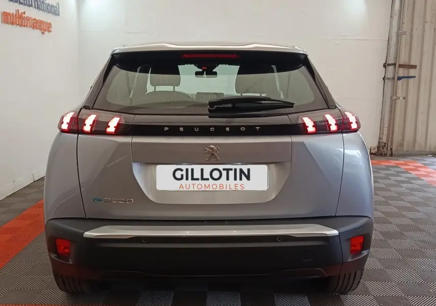 Vue arrière d'un Peugeot E-2008 électrique gris clair avec feux LED caractéristiques allumés en intérieur.