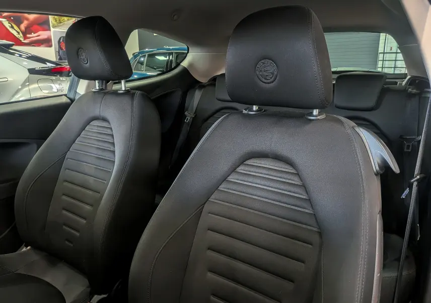 Gros plan sur les sièges avant noirs en tissu de l'Alfa Romeo MiTo 1.3 JTDm 95 CH Super de 2018 avec logo brodé sur les appuie-têtes.