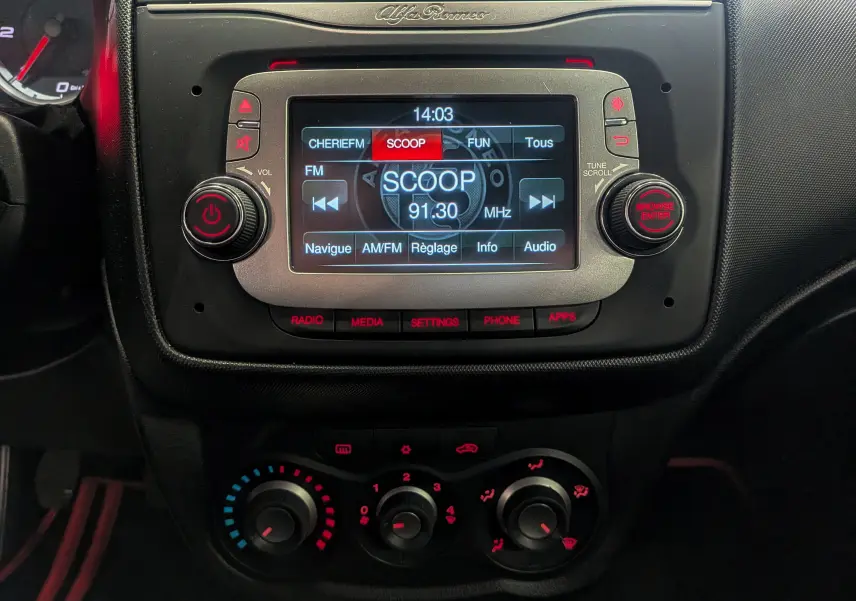Gros plan sur la console centrale de l'Alfa Romeo MiTo rouge, affichant l'écran multimédia et les commandes de climatisation.