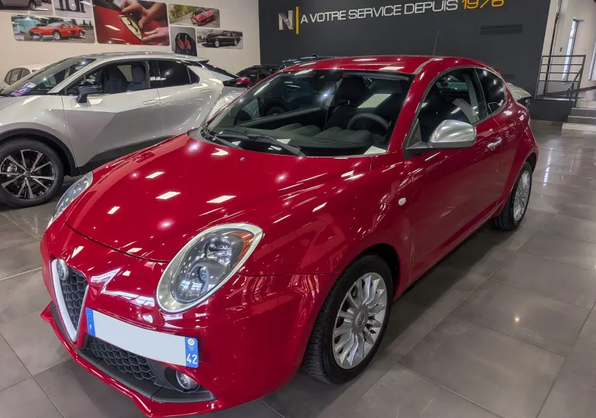 Alfa Romeo MiTo rouge Alfa vue 3/4 avant droit en intérieur avec rétroviseurs argentés et jantes alliage.