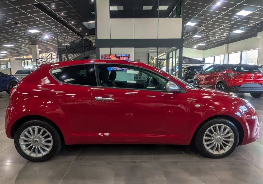 Profil côté gauche de l'Alfa Romeo MiTo rouge Alfa de 2018, avec jantes alliage et poignées chromées visibles en showroom.