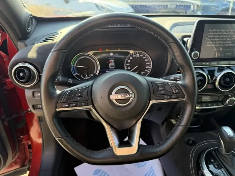 Vue intérieure centrée sur le volant cuir noir du Nissan Juke rouge Fuji avec tableau de bord et écran tactile visibles.
