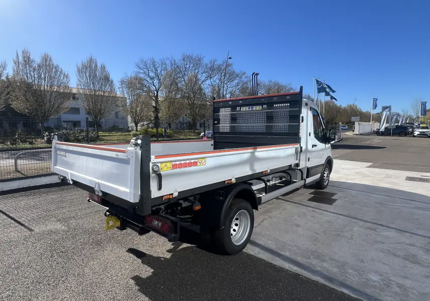 Vue 3/4 arrière droite du Ford Transit Chassis Cabine blanc avec benne et coffre, roues jumelées et grille de protection noire.