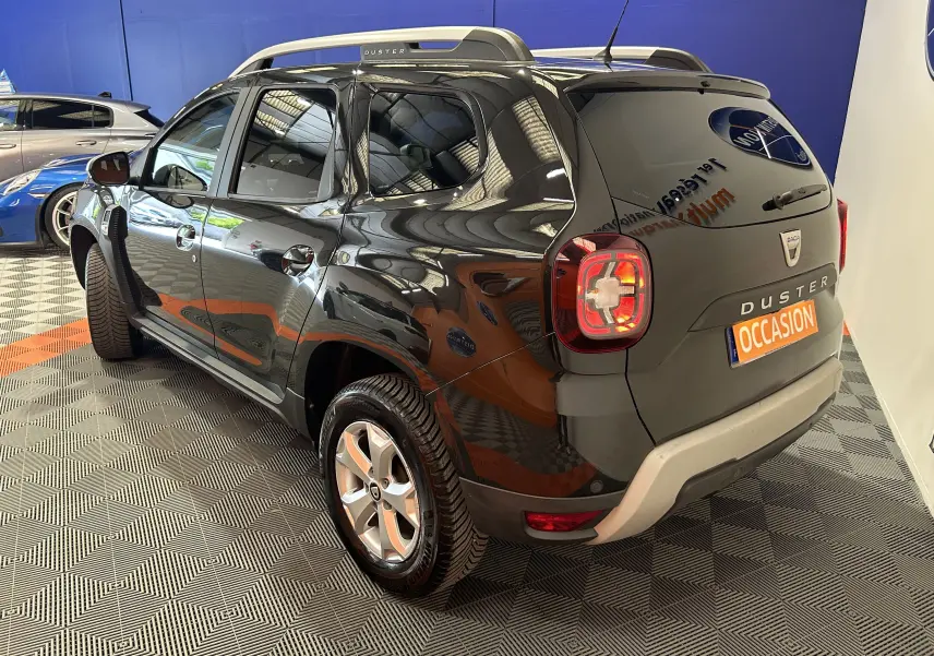 Vue 3/4 arrière droite du Dacia Duster noir avec feux arrière allumés et plaque "OCCASION" visible.