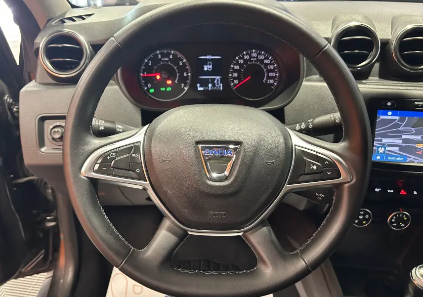 Vue centrée sur le volant noir du Dacia Duster 2018 avec tableau de bord et écran GPS visible à droite.