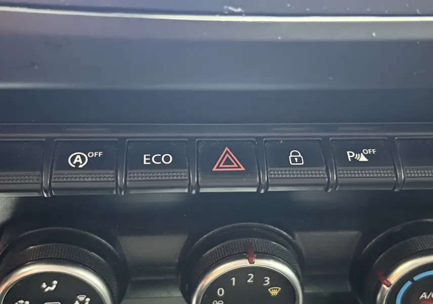 Gros plan sur les commandes centrales du tableau de bord du Dacia Duster noir, avec boutons ECO, alerte et verrouillage.
