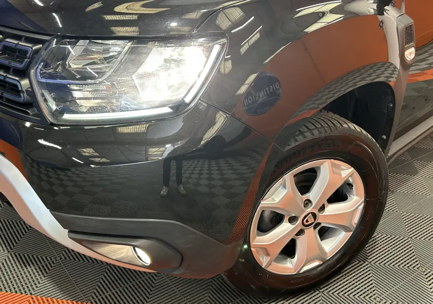 Gros plan sur l'avant droit noir du Dacia Duster 2018, mettant en valeur le phare allumé et la jante alliage.