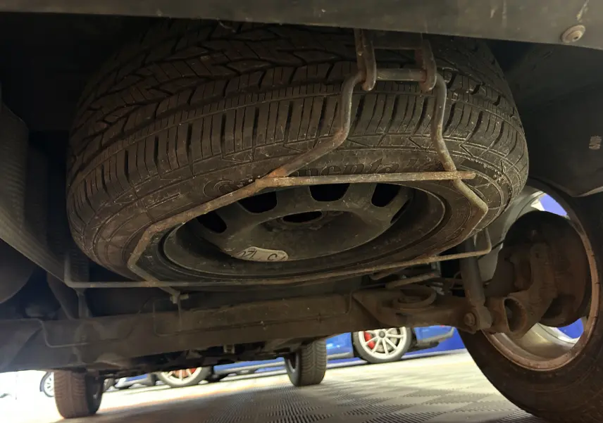 Vue en contre-plongée sous un Dacia Duster noir, montrant la roue de secours fixée sous le châssis arrière.