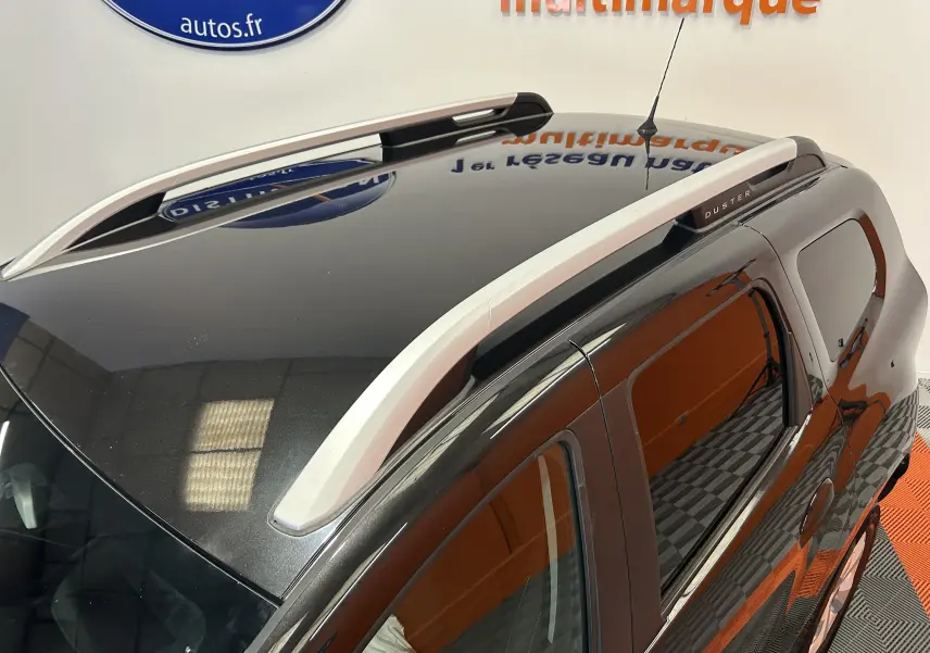Vue en plongée du toit noir brillant d’un Dacia Duster avec barres de toit argentées et vitres teintées.
