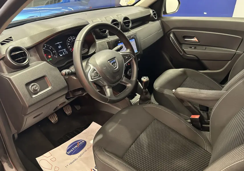 Vue intérieure côté conducteur du Dacia Duster noir 2018, montrant le volant, la console centrale et les sièges en tissu.