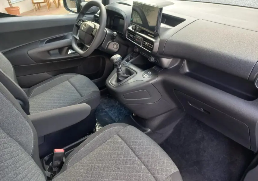 Vue intérieure côté conducteur de l’Opel Combo Life 2025, montrant le tableau de bord noir et les sièges gris tissu.