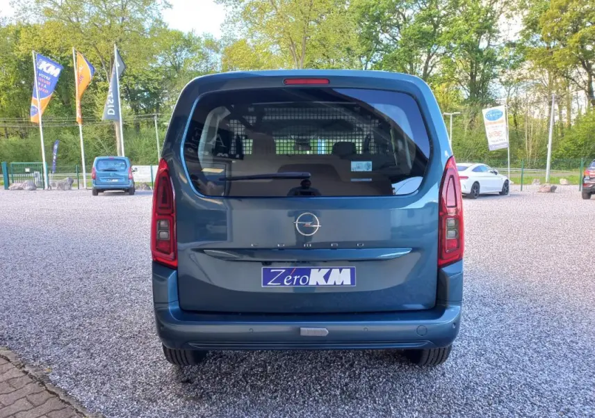 Vue arrière d'un Opel Combo Life M bleu 2025 avec hayon vitré et feux arrière verticaux, stationné sur un sol gravillonné.