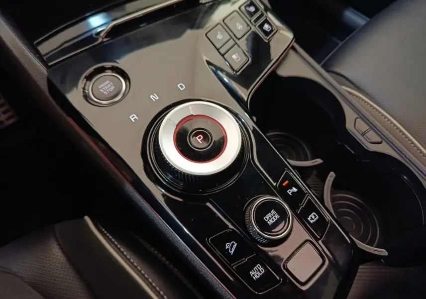 Gros plan sur la console centrale noire brillante du Kia Sportage 2022 avec sélecteur rotatif et boutons de contrôle.