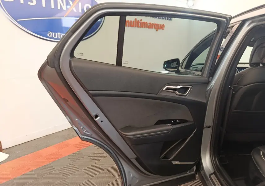 Vue intérieure côté gauche de la porte arrière ouverte d'un KIA Sportage gris clair avec garniture noire et détails chromés.