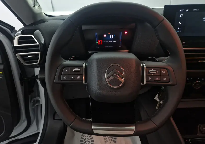 Vue rapprochée du volant cuir noir du Citroën C4 blanc Okenite 2025 avec commandes intégrées et tableau de bord numérique.