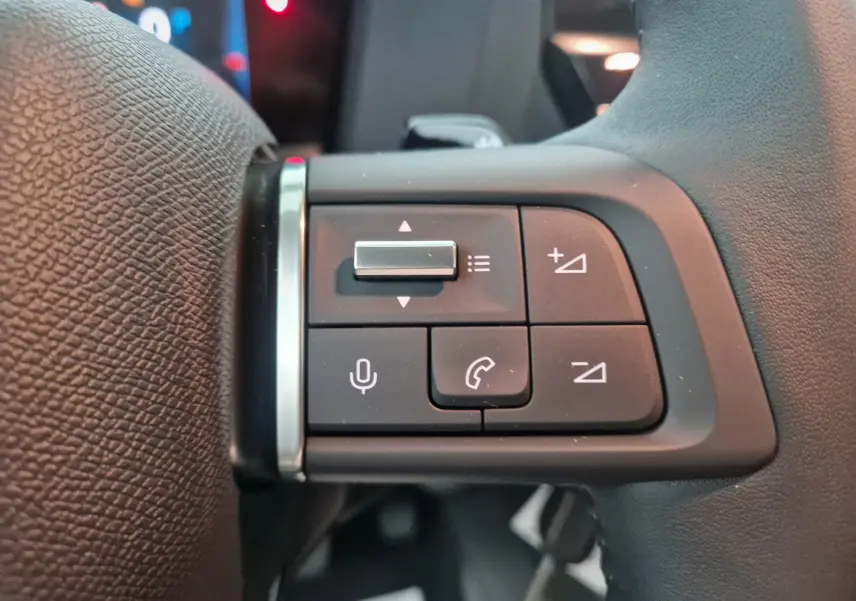 Gros plan sur les commandes du volant à gauche d'une Citroën C4 Blanc Okenite 2025, boutons de volume et téléphone visibles.