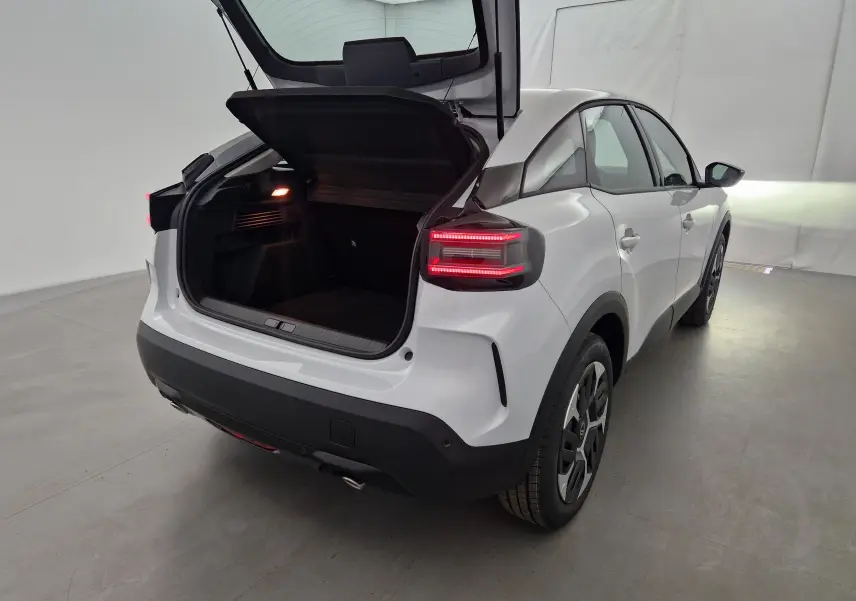 Vue arrière droite d'une Citroën C4 blanc Okenite 2025 avec coffre ouvert et feux arrière allumés dans un studio.