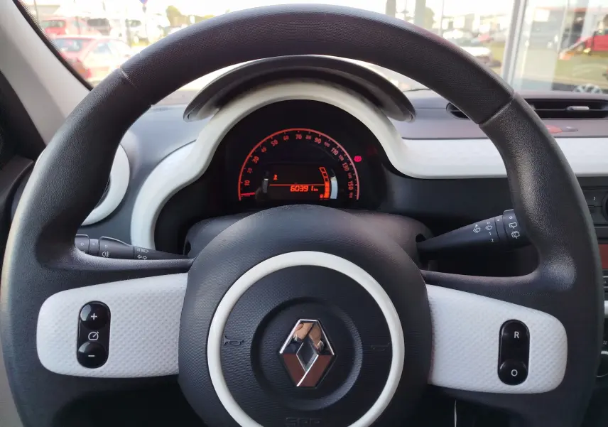 Vue intérieure centrée sur le volant noir et blanc de la Renault Twingo 2016 avec tableau de bord numérique rouge.