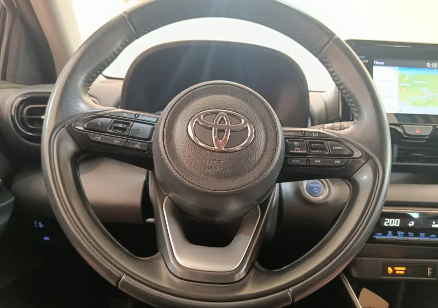 Vue rapprochée du volant cuir multifonctions noir de la Toyota Yaris Hybride 116h avec tableau de bord et écran tactile visibles.