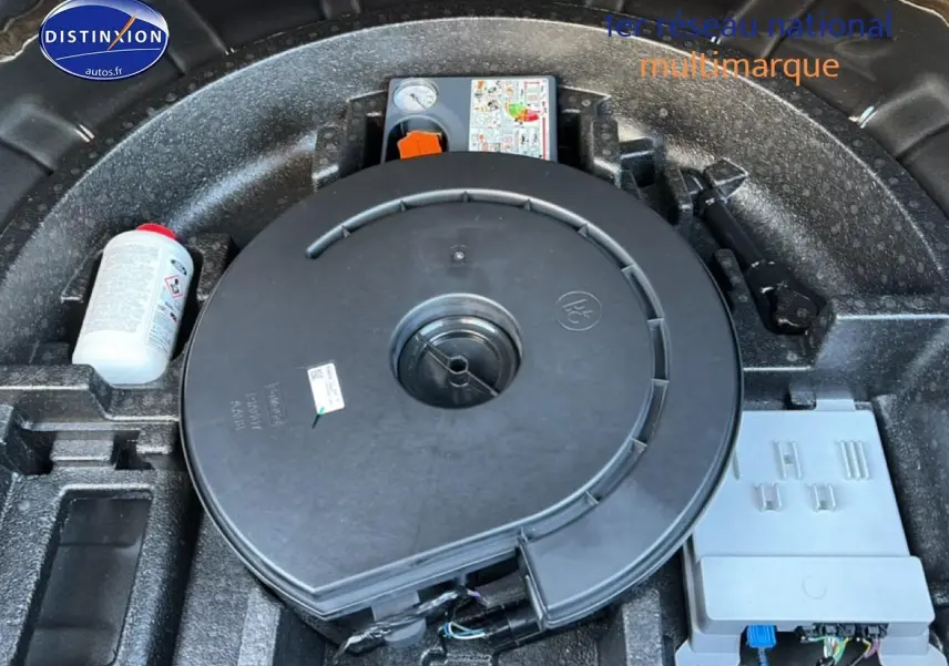 Vue rapprochée du coffre montrant la roue de secours et le kit de réparation sur fond noir.