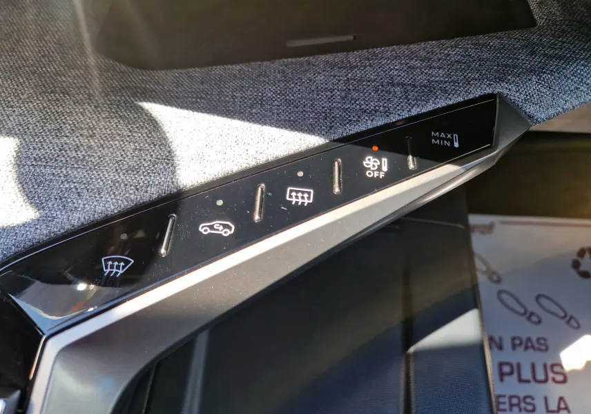 Gros plan sur les commandes de climatisation du Peugeot 3008 gris titane, avec boutons tactiles rétroéclairés et tissu gris en arrière-plan.