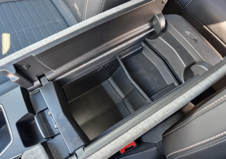 Vue plongeante sur le rangement central ouvert du Peugeot 3008 1.2 HYBRID 145 gris titane, intérieur noir avec surpiqûres claires.