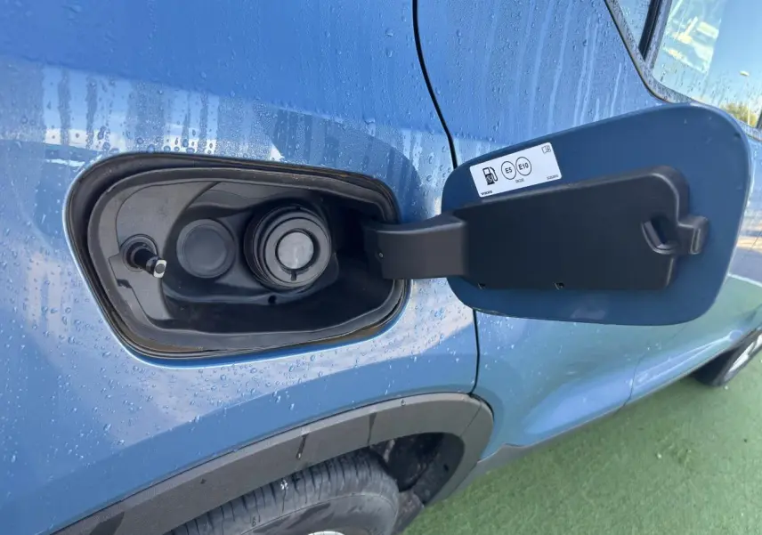 Gros plan sur la trappe à carburant ouverte côté gauche d'un Volvo XC40 Fjord Blue Metal avec gouttes d'eau.