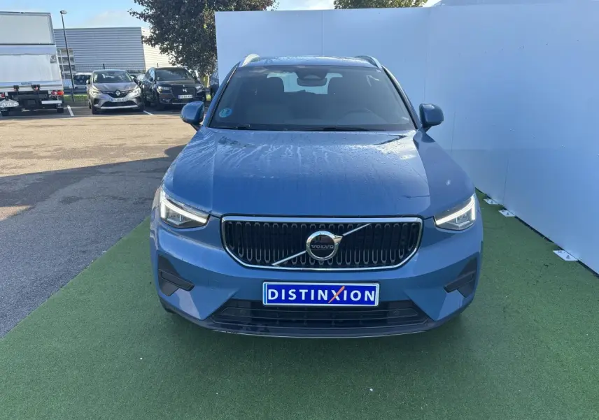Vue frontale du Volvo XC40 Fjord Blue Metal 2024 avec calandre noire et logo centré sur fond vert.