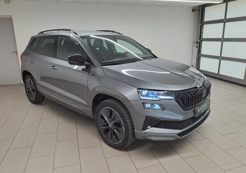 Vue 3/4 avant du Skoda Karoq gris graphite 2025 avec phares allumés et jantes spécifiques Sportline.