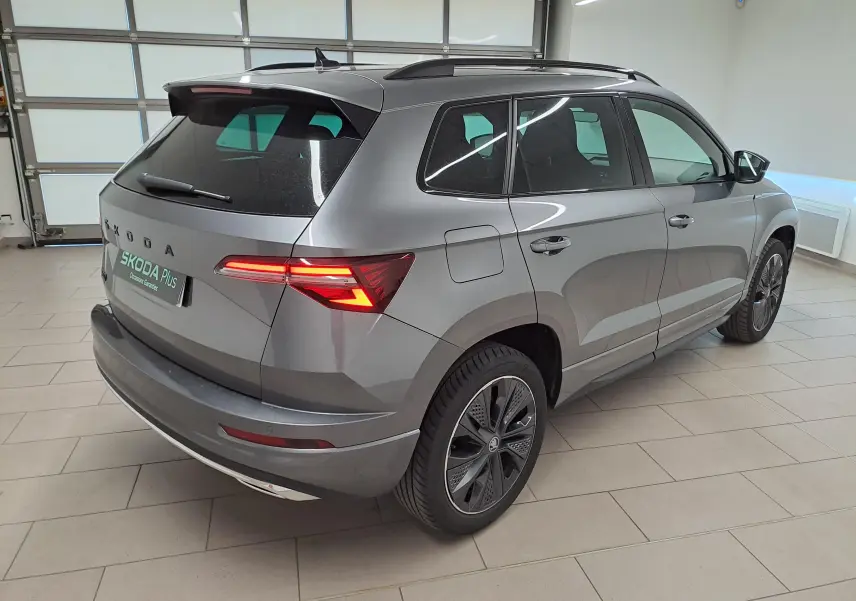 Vue 3/4 arrière droite du Skoda Karoq gris graphite métallisé avec feux arrière allumés dans un garage.