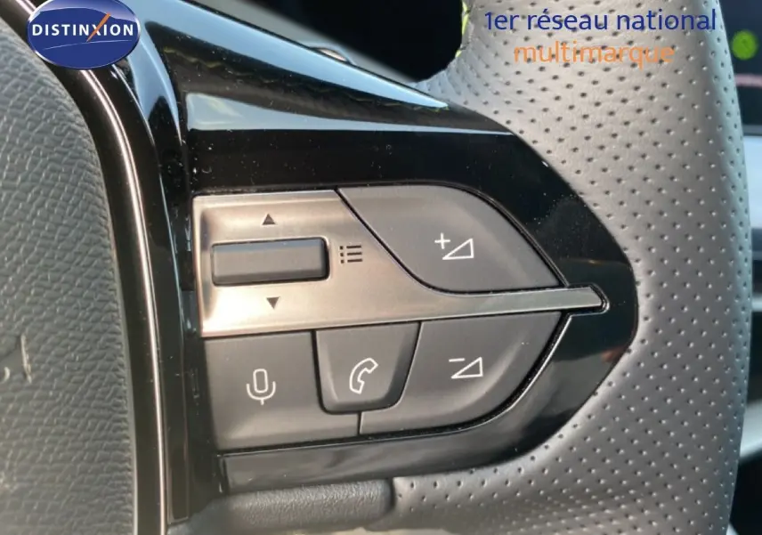 Gros plan sur les commandes de volume et téléphone du volant perforé d’une Peugeot 308 Hybrid blanche.