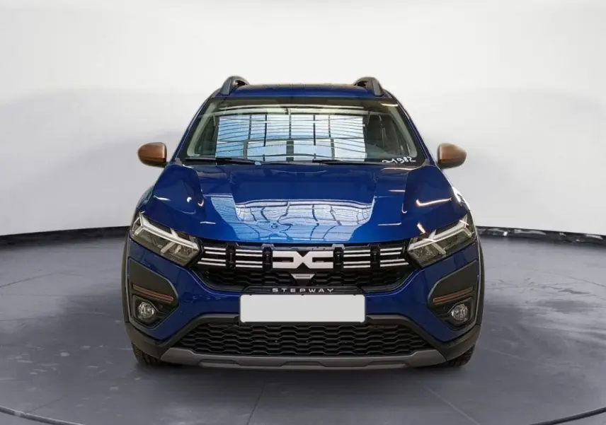 Vue frontale d'une Dacia Sandero Stepway TCE 90 bleu Iron avec calandre noire et détails bronze sur les rétroviseurs.