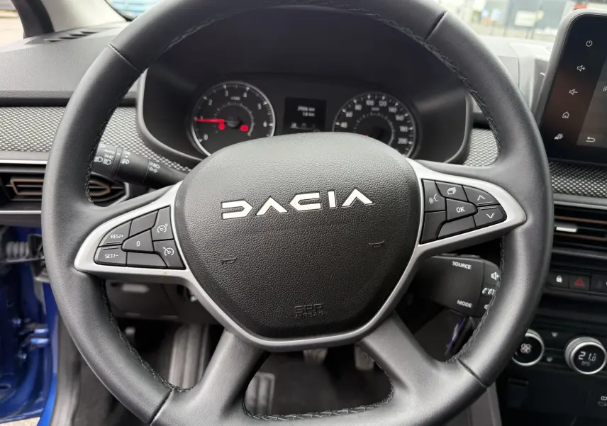 Vue rapprochée du volant noir de la Dacia Sandero Stepway 2025, avec commandes intégrées et tableau de bord en arrière-plan.