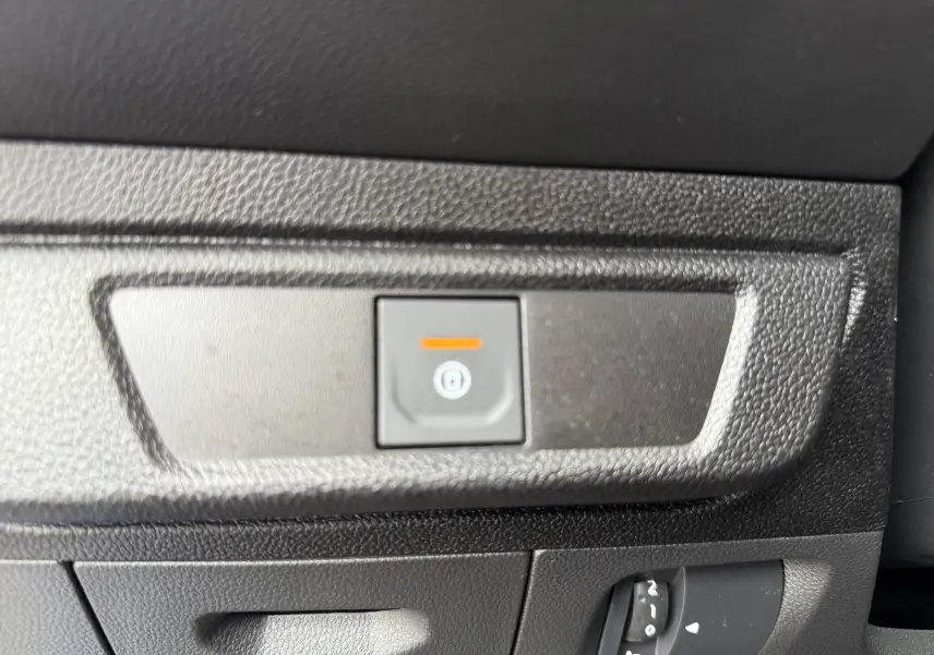 Gros plan sur le bouton de frein à main électrique et la molette de réglage des phares dans l’habitacle noir du Dacia Sandero Stepway bleu Iron.