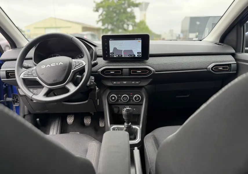 Vue intérieure avant du tableau de bord de la Dacia Sandero Stepway 2025 avec écran tactile et volant multifonction noir.