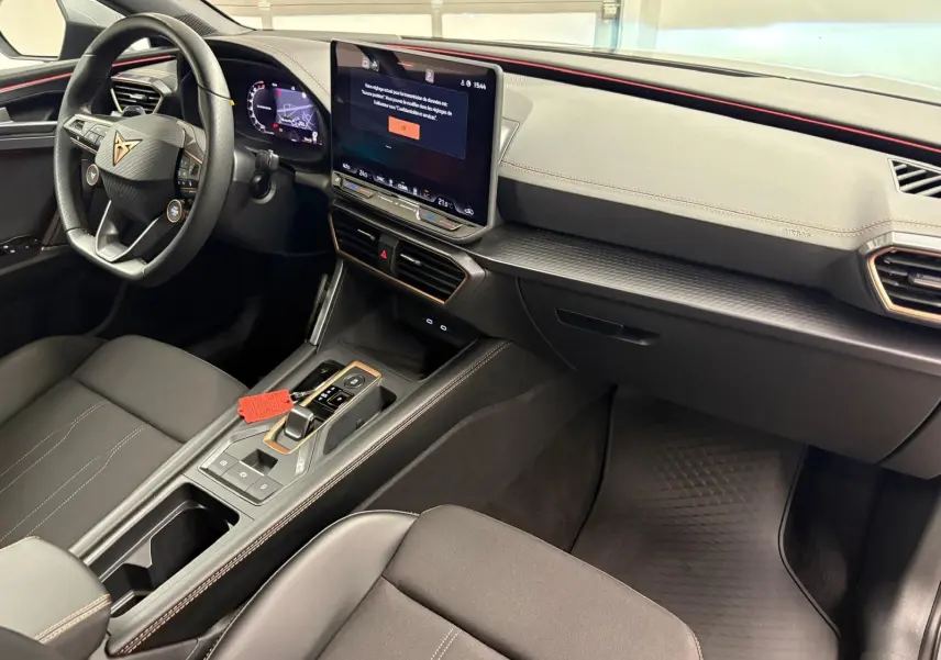 Intérieur de la CUPRA Leon 2025 vu côté passager, tableau de bord noir avec écran central tactile et volant sport.