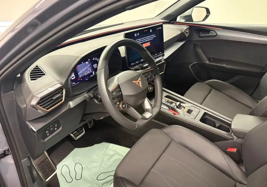 Vue intérieure côté conducteur de la CUPRA Leon 2025 gris Graphène, avec volant multifonction et écran central tactile.