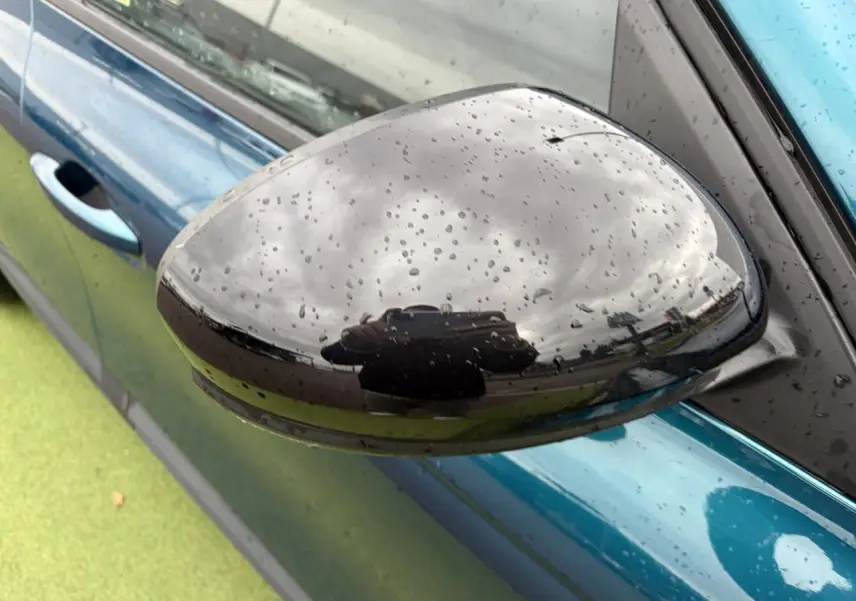 Rétroviseur droit noir brillant avec gouttes d'eau sur Renault Arkana bleu Zanzibar, vue rapprochée côté conducteur.