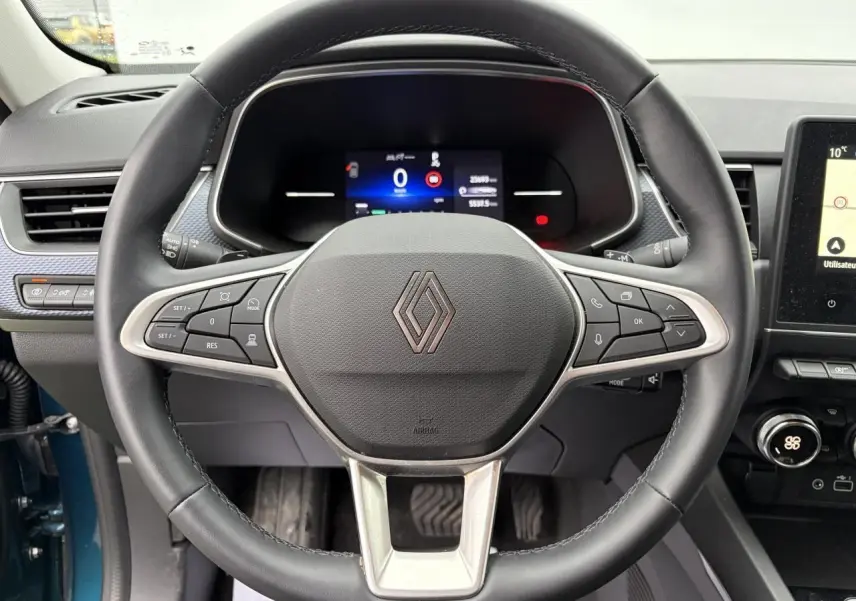 Vue intérieure centrée sur le volant noir de la Renault Arkana 2025 avec tableau de bord numérique et détails argentés.