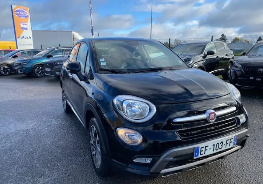 Vue 3/4 avant d'un FIAT 500X Cross noir 2016 avec calandre chromée et feux ronds allumés sur parking.