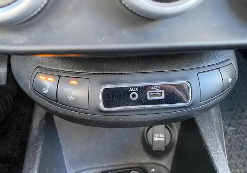 Vue rapprochée de la console centrale noire du Fiat 500X 2016, avec boutons de sièges chauffants et ports AUX et USB.