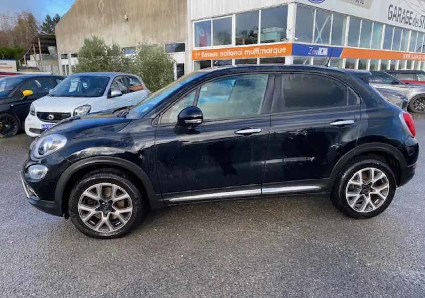 Profil côté gauche d'un Fiat 500X Cross noir 2016 avec jantes alliage et détails chromés sous un ciel clair.
